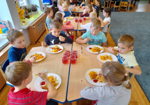 Dzieci siedzą przy stolikach jedzą obiad.